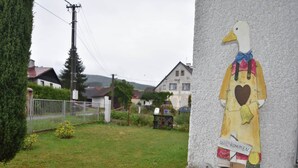 A garden with a large bird sculpture, a white fence, and houses in the background. - Serene Holiday Home in Mladé Buky with small pool, Trampoline & Skiing Nearby (Mladé Buky)