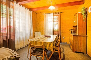 Une cabane en bois chaleureuse, avec une table à manger, des chaises et un petit coin cuisine.