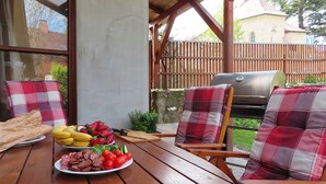 An outdoor patio with a wooden table, a grill, and a view of a backyard. - Mountain Home with Garden (Černý Důl)