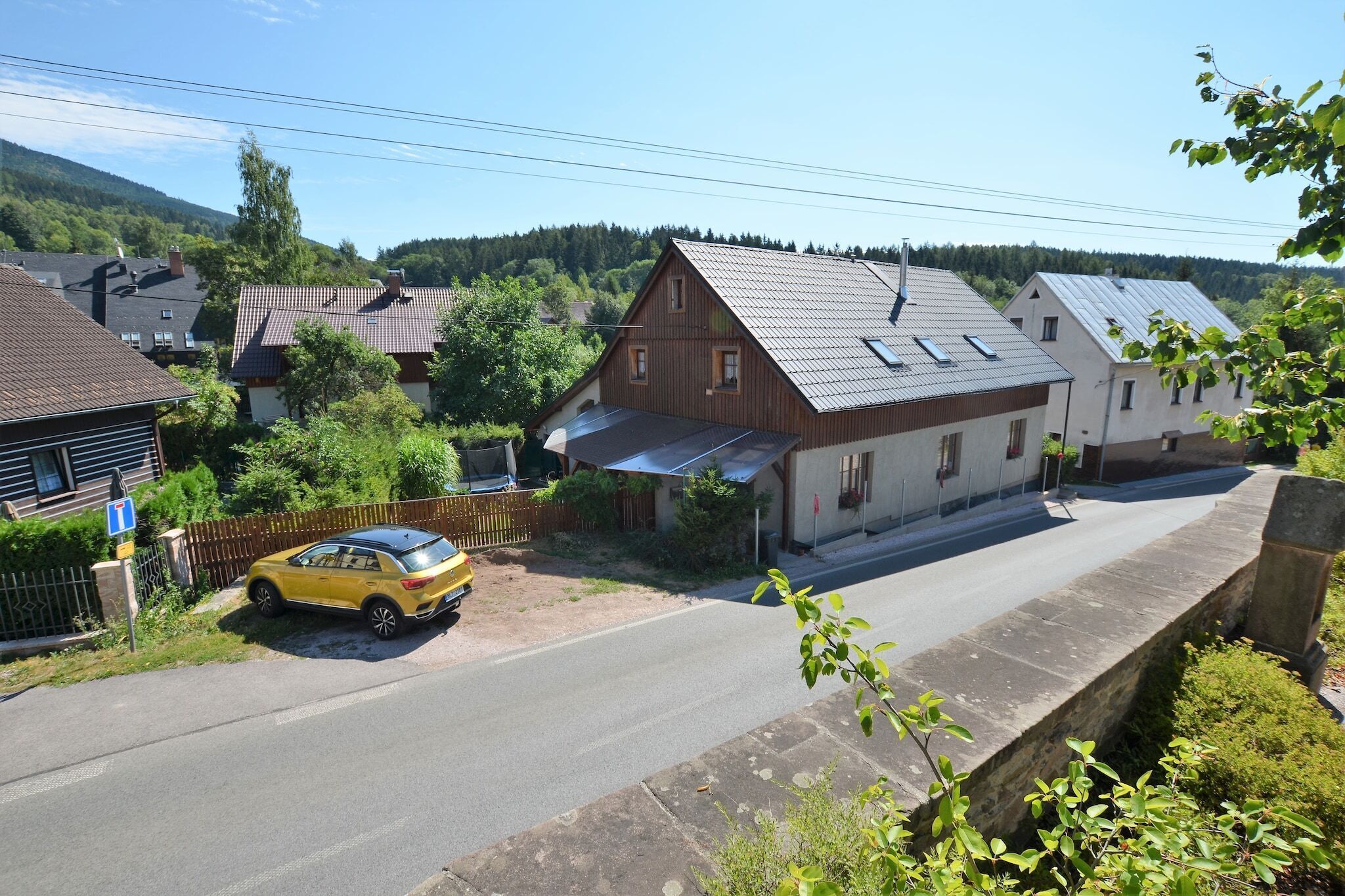 A residential street with houses, a yellow car parked on the side, and a stone wall.