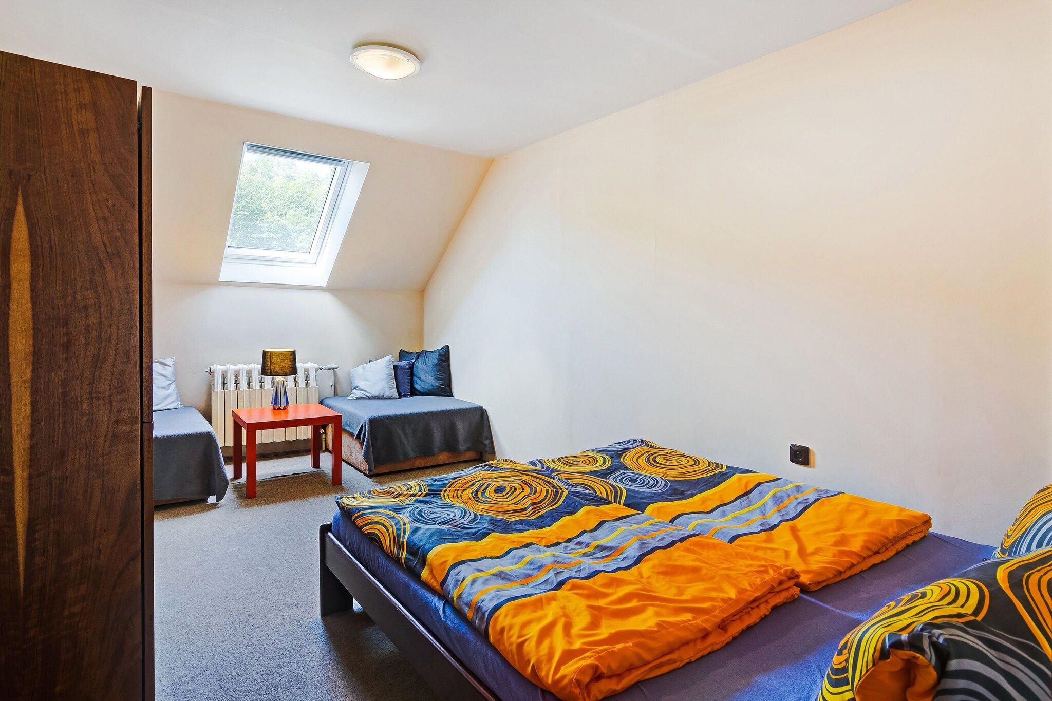 A bedroom with a large bed, a smaller bed, a desk, and a chair. There is a window providing natural light.