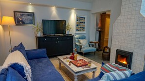 A living room with a sofa, a coffee table with books and a bottle, a television, and a fireplace. - San Rocco -  a dog friendly cottage that sleeps 6 guests  in 3 bedrooms (Bembridge)