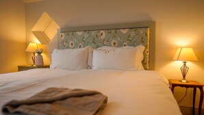 A neatly made bed with white linens, two bedside lamps, and a floral-patterned headboard. - San Rocco -  a dog friendly cottage that sleeps 6 guests  in 3 bedrooms (Bembridge)