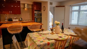 A dining area with a table set for four, surrounded by wicker chairs, and a kitchen area with red cabinets and a stove. - San Rocco -  a dog friendly cottage that sleeps 6 guests  in 3 bedrooms (Bembridge)