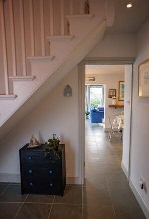 Una escalera conduce a una sala de estar con un sofá azul, un modelo de velero pequeño y una planta sobre un mueble negro.
