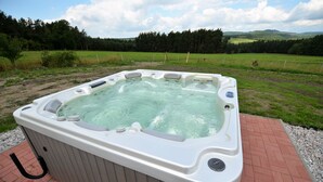 Un bain à remous installé à l’extérieur, avec un champ verdoyant et des arbres en arrière-plan.