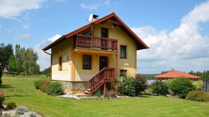Une maison à deux étages dotée d’un balcon, entourée d’une pelouse et d’un jardin bien entretenus.