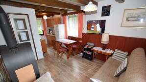 Un salon chaleureux avec une cheminée, des meubles en bois, un téléviseur et un coin cuisine doté de placards en bois et d’un réfrigérateur.