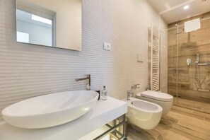 A modern bathroom with a large oval sink, a bidet, and a glass-enclosed shower.