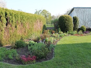 Stroll through the beautifully maintained garden, featuring a variety of plants and flowers, including a neatly trimmed hedge and a flower bed with blossoms.