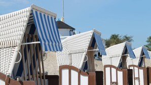 Strandhütten mit Streifenmarkisen und Holztüren, anordiniert in Reihen auf einem Sandstrand.