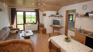 Ein gemütliches Wohnzimmer mit einer Couch, einem Esstisch mit Stühlen, einem Fernseher und einer Küchenzeile mit Spüle und Regalen.