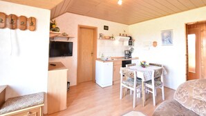 Ein gemütliches Wohnzimmer mit einer Couch, einem Esstisch mit Stühlen, einem an der Wand befestigten Fernseher und einer Küchenzeile mit Kühlschrank, Mikrowelle und Spüle.