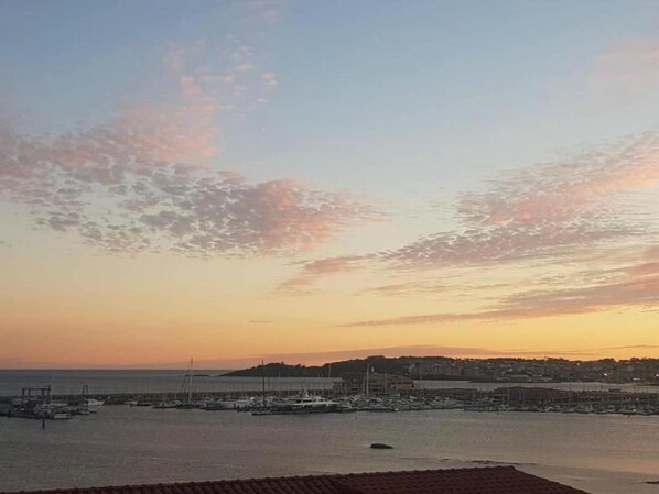 Un puerto costero con barcos amarrados, cielo despejado y un paisaje montañoso distante.