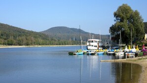 Un lago tranquilo con varias embarcaciones amarradas en la orilla, rodeado de colinas y árboles.