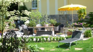 Un patio al aire libre con mobiliario de mimbre, un paraguas amarillo y plantas en macetas.