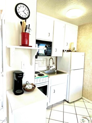 A compact kitchen with white cabinets, a stove, a sink, a refrigerator, and a clock on the wall.