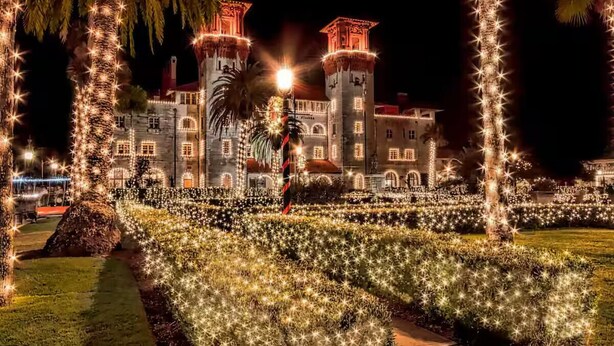 Un edificio parecido a un castillo con múltiples torres, rodeado de un jardín bien iluminado con luces en forma de estrella.