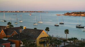Un pueblo costero con barcos de vela amarrados a lo largo de la orilla, con edificios residenciales y un muelle que se adentra en el mar.