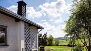 Ein Haus mit einer Steinterrasse, einem Schornstein und Blick auf eine grüne Landschaft.