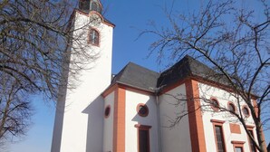 Eine Kirche mit einem hohen Glockenturm und einer weißen Fassade mit roten Akzenten.