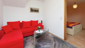 A modern living room with a red sofa, a glass coffee table, and a painting on the wall.