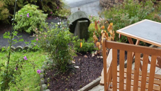 A wooden bench and table in a garden with a hot tub and a stone structure.