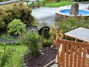 A wooden bench and table in a garden with a hot tub and a stone structure. - Einladende Ferienwohnung in Muellenborn Eifel (Gerolstein)