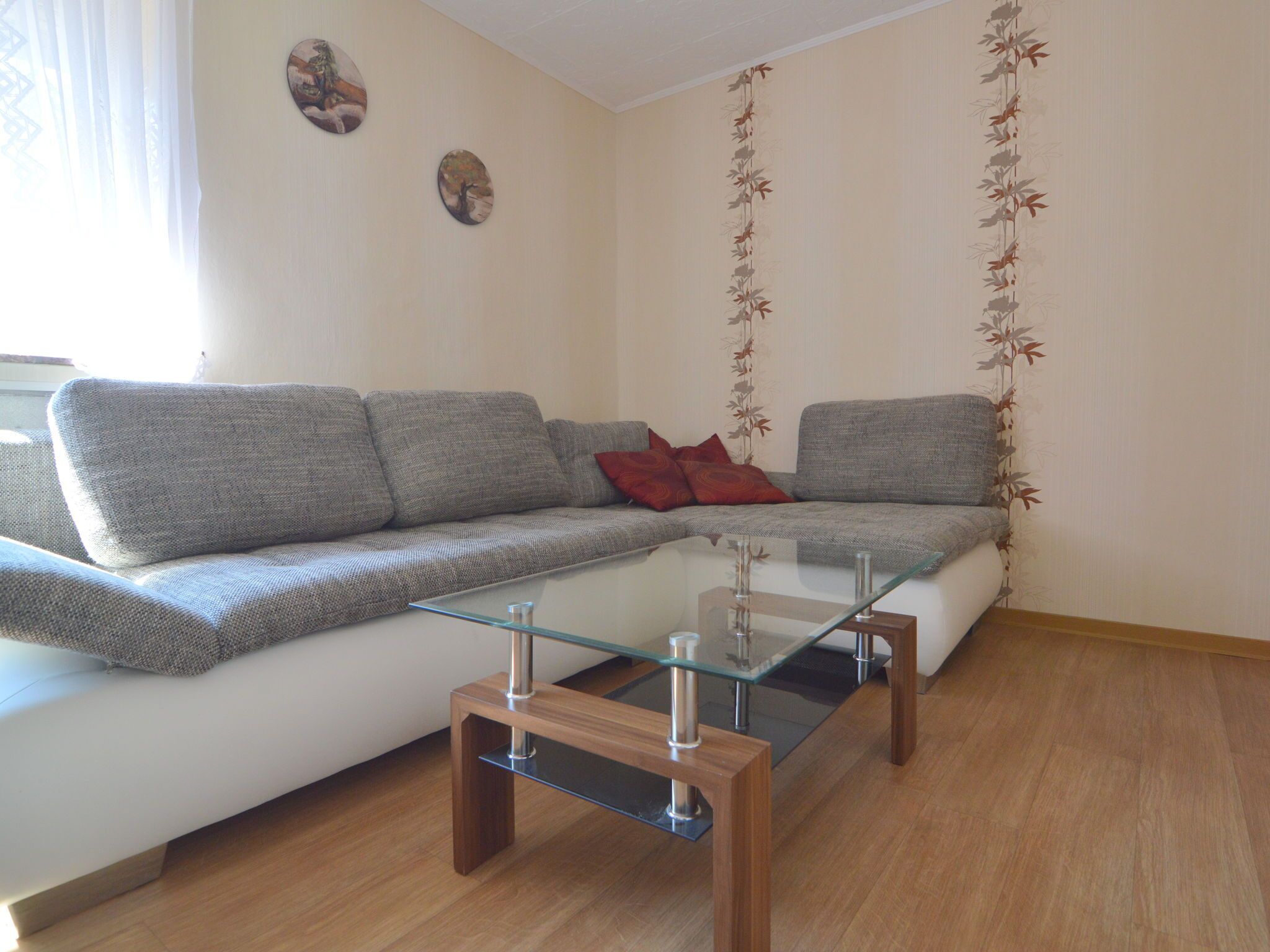 Ein modernes Wohnzimmer mit grauem Sofa, einem Glastisch und Holzboden.
