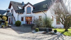 A two-story house with a steeply pitched roof, a front porch, and a driveway leading to a parked car. - Flat in Beltheim (Germany) with pool (Beltheim)