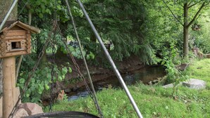 A wooden birdhouse attached to a tree, a metal grill, and a small stream in a wooded area.