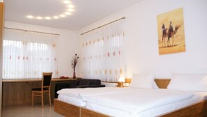 A hotel room with a wooden bed, a desk, a chair, and a painting of camels on the wall.