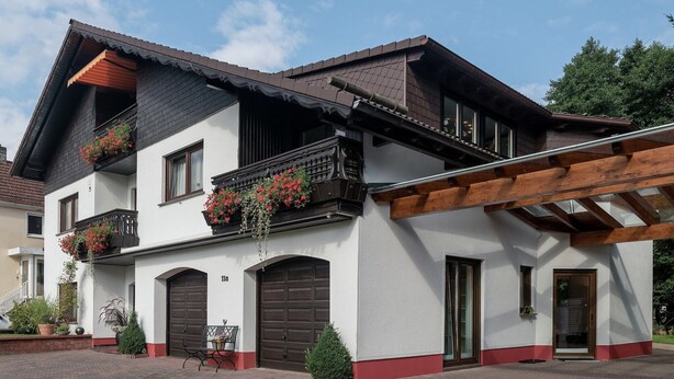 A two-story building with a white facade, dark brown roof, and wooden balcony railings.