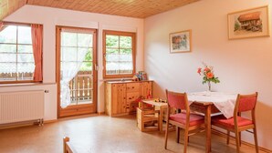 A cozy room with a wooden ceiling, a dining table with chairs, a radiator, and a window with curtains. - Schwarzwald-Ferienwohnung auf dem Bauernhof (Schuttertal-Regelsbach)