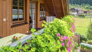 A wooden cabin with large windows, a porch with a table, and a garden with flowers. - Schwarzwald-Ferienwohnung auf dem Bauernhof (Schuttertal-Regelsbach)