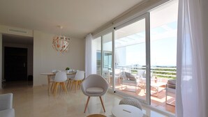 A modern living room with a dining area, large sliding glass doors leading to a balcony, and a view of the cityscape. - Belvilla by OYO Alcazaba Lagoon (Casares)