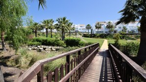 A wooden boardwalk leading to a building complex with a clear sky. - Belvilla by OYO Alcazaba Lagoon (Casares)