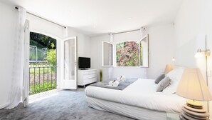 Un dormitorio con una cama grande, televisión y balcón con vistas a zonas verdes.