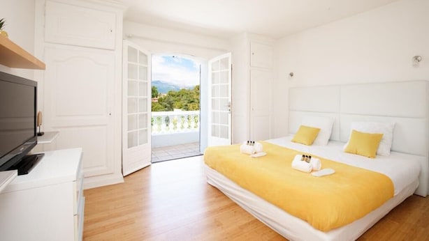 Un dormitorio con cama, televisión y puerta abierta que da a un balcón.