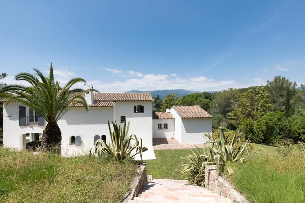 A white building with a tiled roof, surrounded by greenery and a clear sky.