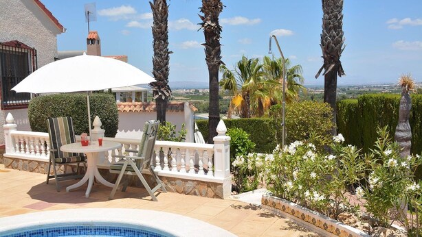 A poolside area with a white umbrella, a round table, and chairs.