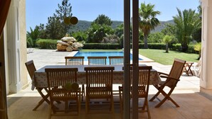Zona junto a la piscina con mesa y sillas, vista a la montaña y un jardín cuidado.