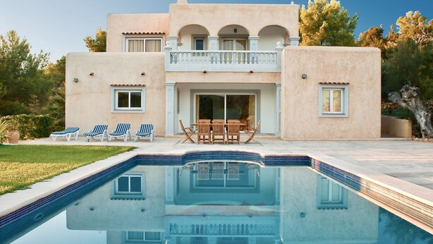Una casa de dos pisos con piscina, balcón y patio con mobiliario exterior.