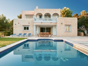 Una casa de dos pisos con piscina, balcón y patio con mobiliario exterior.