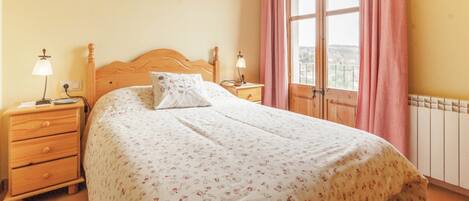 Un dormitorio con cama de madera, dos mesitas de noche con lámparas, una ventana con cortinas rosadas y un radiador.