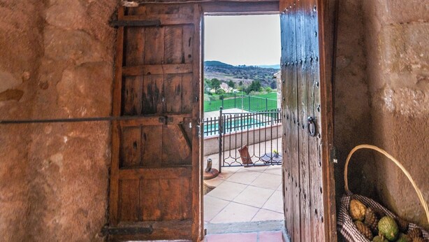 A rustic wooden door leading to an outdoor area with a pool and a view of green fields.