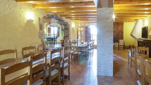 A spacious dining area with wooden tables and chairs, stone walls, and a large pillar.