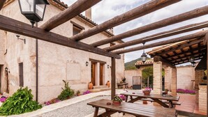 An outdoor patio area with wooden benches and tables, surrounded by stone walls and potted plants.