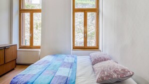 Ein Schlafzimmer mit einem Bett, zwei Fenstern, einem Heizkörper und einer Holzkommode.