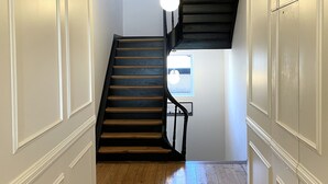 A hallway with a wooden floor, white walls, and a black staircase. - Apartment Cypress (Stutzheim-Offenheim)